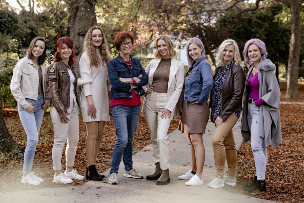 Das Team von Kimm Hair Studio in verschiedenen Outfits, die auf einem Weg stehen, umgeben von herbstlichen Blättern. Foto by Michaela Begsteiger